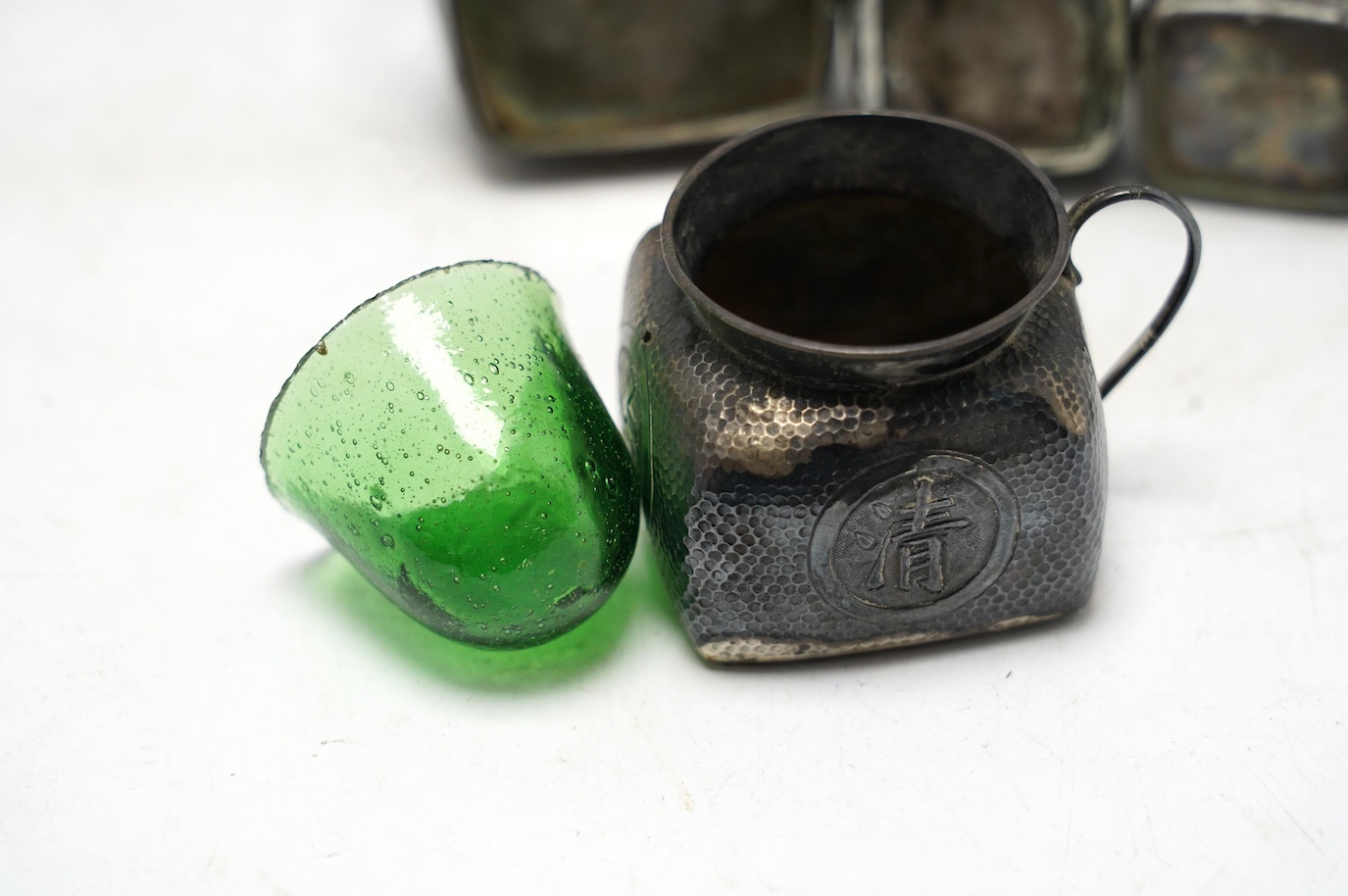 A Chinese embossed white metal cylindrical jar and cover, 11.2cm, and a similar white metal four piece cruet set. Condition - poor to fair